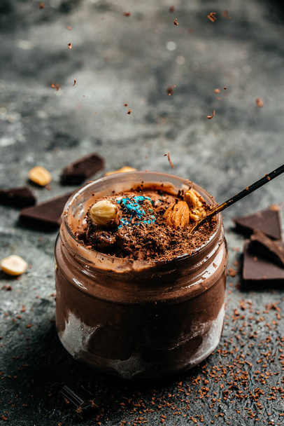 Serving homemade chocolate ice cream drizzled with chocolate in a glass jar on dark background, vertical image. top view. place for text. - Photo, Image