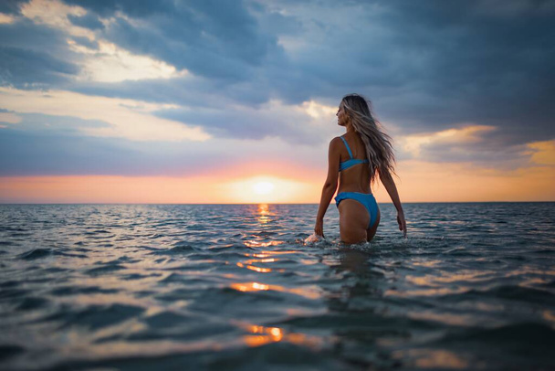 Girl with blond hair in a swimsuit posing against the backdrop of the sunset in the estuary enjoying nature around him - Fotó, kép