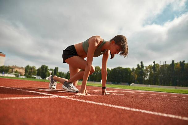 Soustředěná mladá atletka připravená začít závod na stadionu ve dne - Fotografie, Obrázek