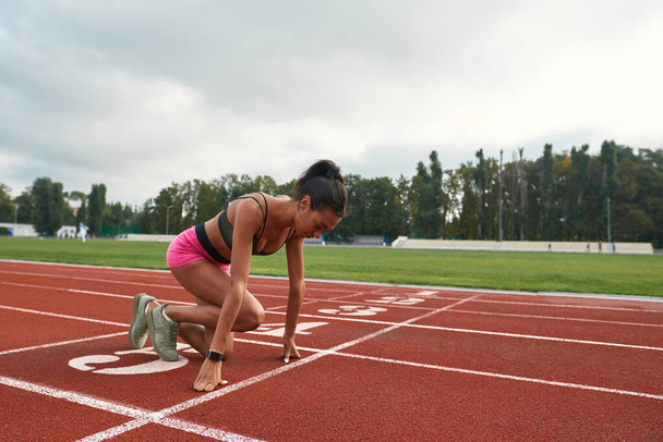 Professional young female runner in sportswear getting ready to start running on track field at stadium - Foto, Imagem