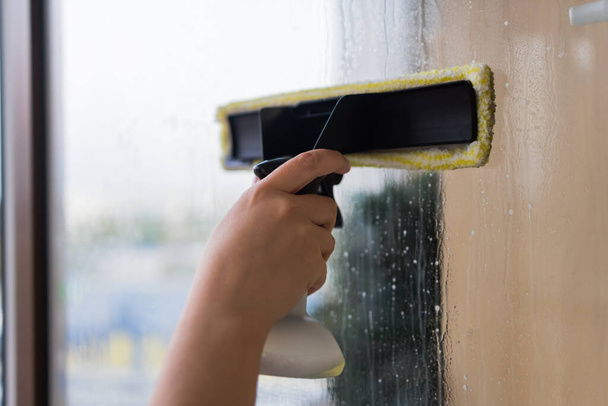 Beautiful young housewife in working clothes washing windows by professional tools at home. - Fotoğraf, Görsel