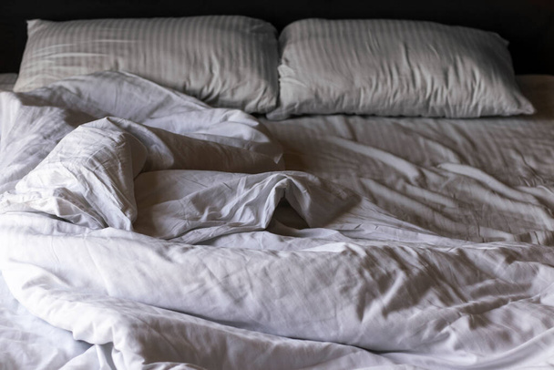 Leeres Bett mit zerknüllter weißer Bettwäsche am Morgen. Dunkles Licht. - Foto, Bild
