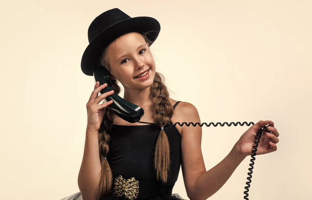 she is listening. new technology. teen girl in hat speak on phone. retro phone. happy childhood. kid has telephone conversation. communication in modern life. child with old fashioned vintage phone - Foto, afbeelding