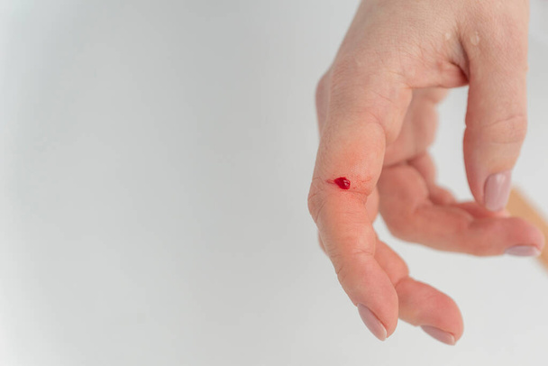Dedo feminino com gota de sangue vermelho. Lesão devido a ações descuidadas com objetos afiados. Sangramento do dedo. - Foto, Imagem