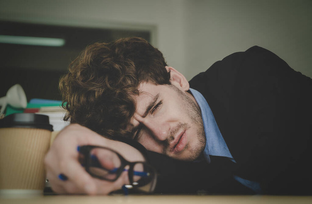 Hombre de negocios sin esperanza descansando en el escritorio de la oficina con emoción de frenesí y cara agotada. - Foto, imagen