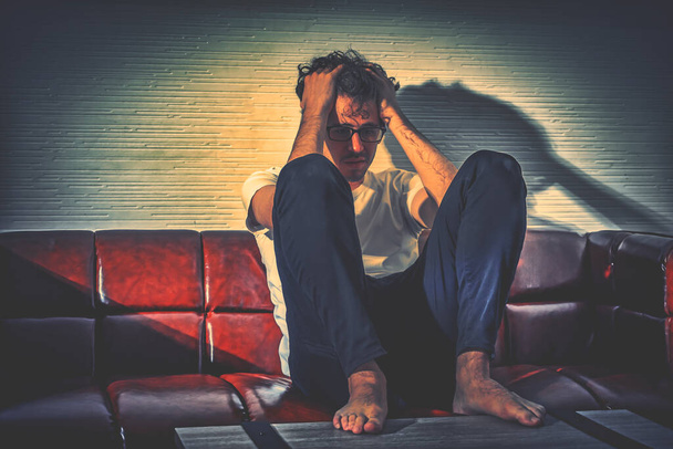 Unglücklicher gestresster Mann, der allein auf einer Couch im Wohnzimmer sitzt und unter Problemen und Schmerzen leidet. - Foto, Bild