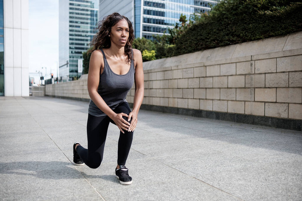 Portrait of mature black woman stretching in the street. She wear activewear and she is in a business environment. - Photo, Image