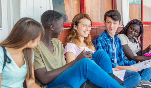 Gruppe von Teenagern gemischter Rassen in der Schule mit Notizbüchern, die lächeln und scherzen. - Foto, Bild