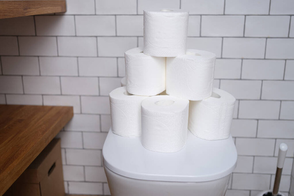 Стопка туалетной бумаги стоит на белом унитазе в ванной крупным планом - Фото, изображение
