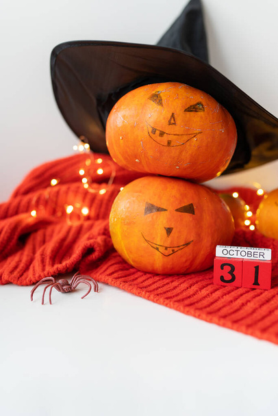 Два гарбуза з пофарбованим обличчям в капелюсі, павук, дерев'яний календар на червоному светрі. Концепція свята 31 жовтня, Хеллоуїн. Красивий боке на фоні
 - Фото, зображення