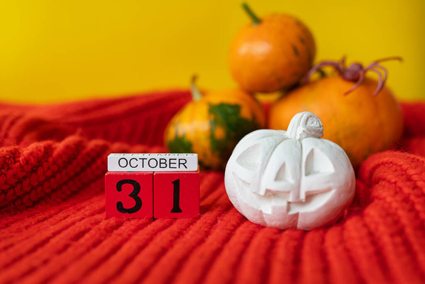 Tegen de achtergrond van een pompoen met een geschilderd gezicht, een spin, een gipsen figuur, een houten kalender op een rode trui. Vakantie concept van 31 oktober, Halloween - Foto, afbeelding