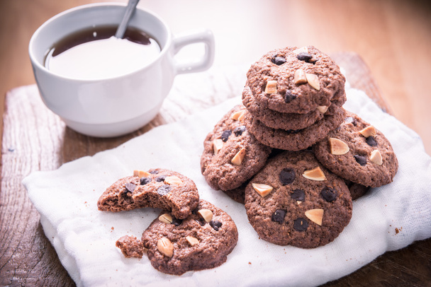 Chocolate chip cookies on napkin and hot tea on wooden table. - Photo, Image