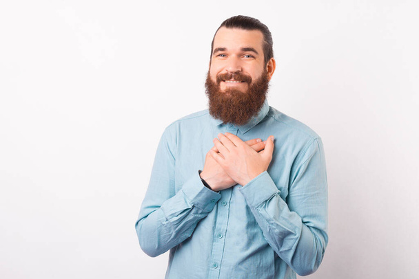 Щасливий молодий бородатий чоловік тримає руки на грудях
. - Фото, зображення