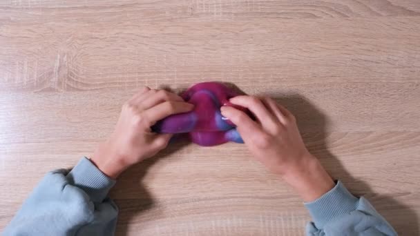 Spiel mit Schleim, Stretching der gooey Substanz für Spaß und Stressabbau. Nahaufnahme und Draufsicht einer weiblichen Hand, die blauen, rosa und lila glänzenden Schleim hält und ihn zusammendrückt. 4K-Video - Filmmaterial, Video