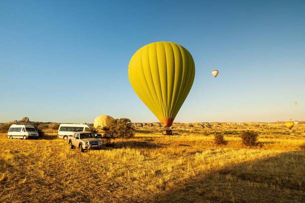 Kaksi kuumailmapalloa nousee ilmaan tai laskeutuu pellolle. Yksi on maassa. Toinen on ilmassa miehistön jäsen ajoneuvossa valmis tukemaan Cappadocia, Turkki - Valokuva, kuva