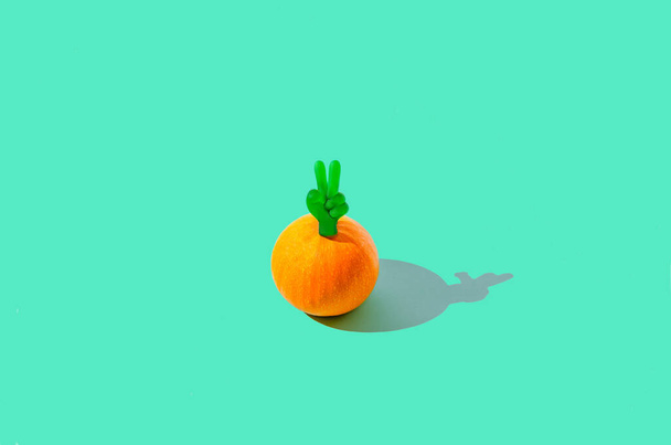 An orange pumpkin on pastel green background with the two fingers peace sign on it. Positive fall vibes creative concept. Funny Halloween artistic design. - Фото, изображение