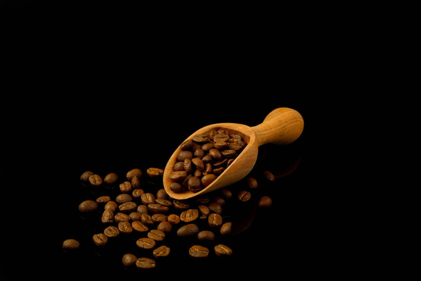 Kaffeebohnen in einer Holzschaufel isoliert auf schwarzem Hintergrund. Geröstete Kaffeebohnen isoliert. Eine hölzerne Schaufel mit Kaffee. - Foto, Bild