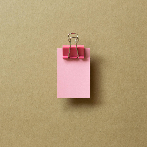 Blocco note bianco rosa appiccicoso e clip in metallo su sfondo marrone. vista dall'alto, copiare lo spazio - Foto, immagini