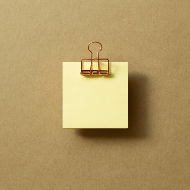 Boş sarı yapışkan not defteri ve kahverengi arka planda metal klipsi. Üst görünüm, boşluk kopyala - Fotoğraf, Görsel