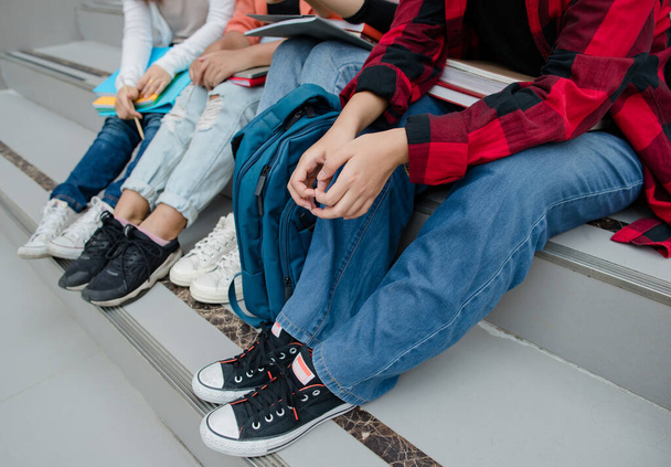 Groep van vier jonge meisjes college studenten benen en sneakers zitten samen in de universiteitscampus buiten. Concept voor onderwijs, vriendschap en het leven van studenten. - Foto, afbeelding