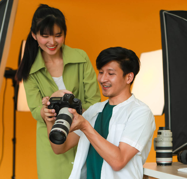Profesional joven fotógrafo masculino sosteniendo la cámara digital y comprobando fotos en la pantalla de la cámara junto con el hermoso modelo joven mientras trabaja en un bonito estudio equipado - Foto, imagen