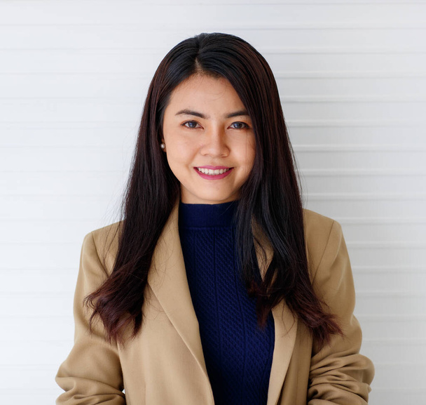 Ritratto orizzontale in primo piano di una giovane donna asiatica attraente e sorridente in abito marrone formale e vestiti blu guardando la fotocamera isolata con sfondo bianco in studio - Foto, immagini