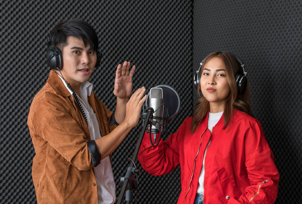 Cieszy etnicznych piosenkarzy płci męskiej i żeńskiej w słuchawkach stojących w studio nagrań muzycznych i patrząc w kamerę. - Zdjęcie, obraz