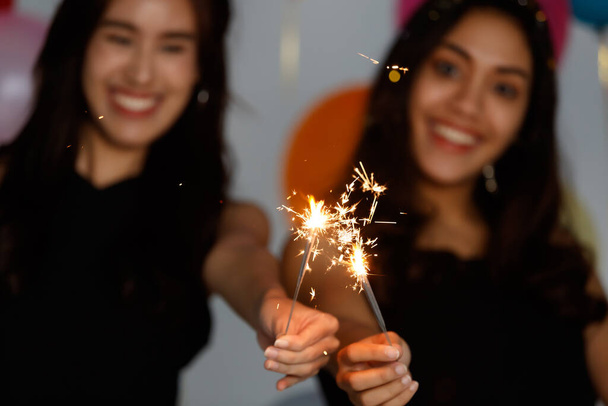 Deux jeunes et belles filles asiatiques sexy dans une robe noire jouant avec de petits feux d'artifice avec plaisir et bonheur dans la fête. - Photo, image