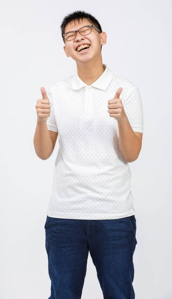 Portrait shot of handsome smiling young boy teenager wearing eyeglasses looking to the camera and showing thumbs up with fingers isolated on white background in the studio. Concept of success - Photo, Image