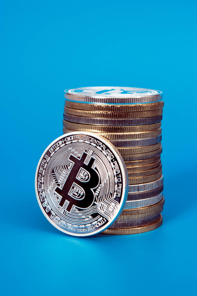 One silver bitcoin and stack of bitcoins over blue background - Zdjęcie, obraz
