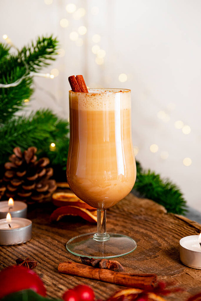 A glass of traditional Christmas drink eggnog on a festive table, vertical photo. Spicy drink made from egg and milk with cinnamon, cardamom. High quality photo - Foto, imagen