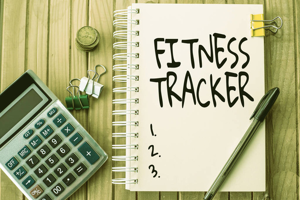Sign displaying Fitness Tracker. Internet Concept device that records a persons daily physical activity Plain Spiral Notebook With Pen Beside Calculator And Coins On Table. - Photo, Image