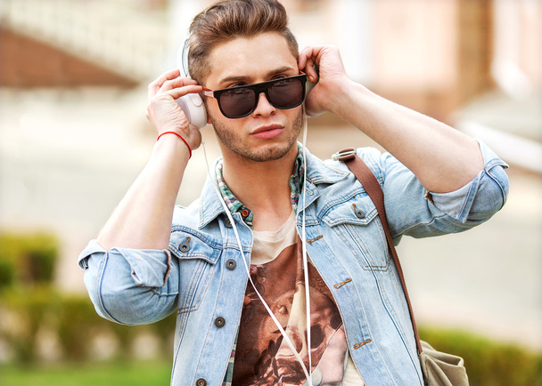 handsome fashion man listening to music on the grass in the park - Foto, Imagen