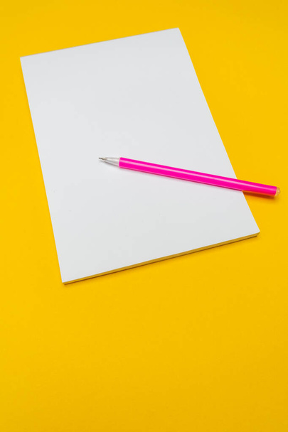 Σημειωματάριο με αντίγραφο χώρου με ροζ στυλό σε κίτρινο φόντο.Απλό φωτεινό φόντο με θέση για κείμενο - Φωτογραφία, εικόνα