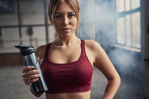 Sportswoman with bottle of water in gym - Foto, afbeelding