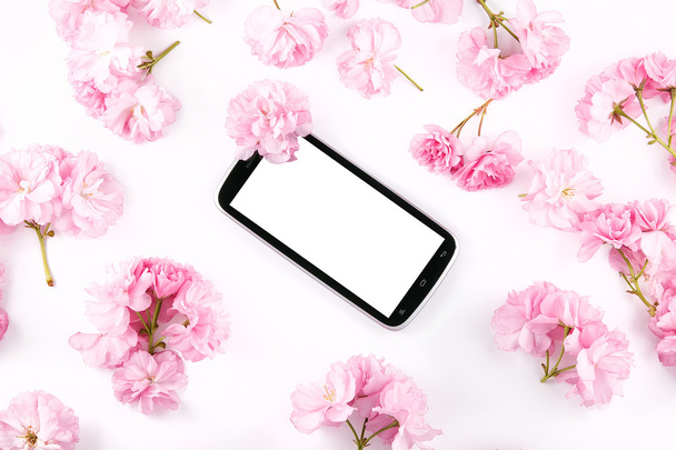 Mobil smart phone surrounded by pink cherry flowers - Photo, Image