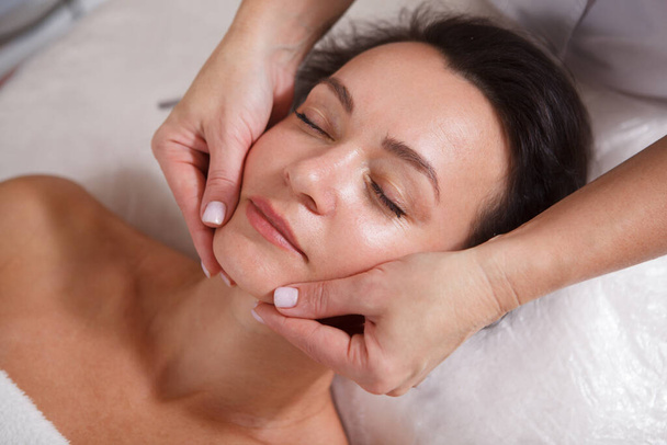 Top view close up of a mature woman getting facial massage by spa salon therapist - Photo, image