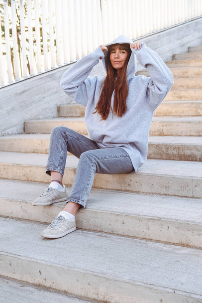 Beautiful woman in grey sweatshirt seats on a stairs. - Foto, afbeelding