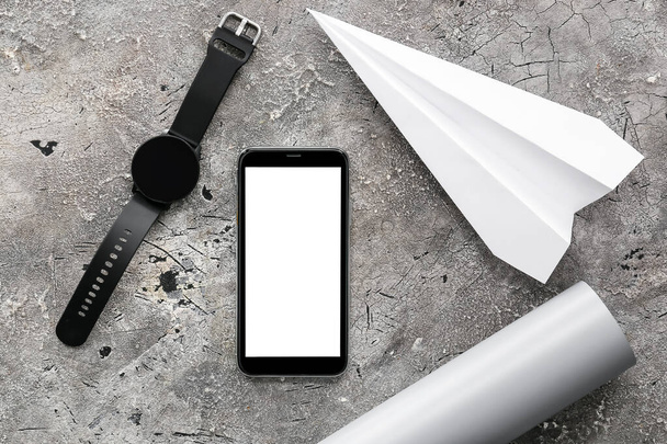 Mobiele telefoon, polshorloge en papieren vliegtuig op grunge achtergrond - Foto, afbeelding