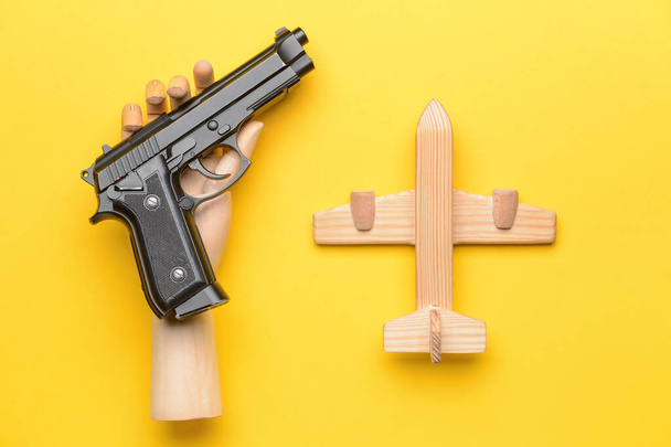 Hand mit Pistole und Holzflugzeug auf farbigem Hintergrund. Konzept der Geiselnahme - Foto, Bild