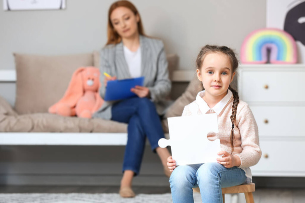 Dziewczynka cierpiąca na zaburzenia autystyczne z kawałkiem układanki w gabinecie psychologa dziecięcego - Zdjęcie, obraz