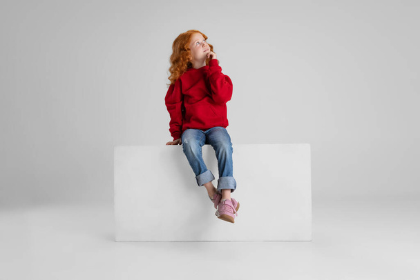 Pienen valkoihoisen punatukkaisen kiharatytön muotokuva, lapsi poseeraa harmaalla studiotaustalla. - Valokuva, kuva