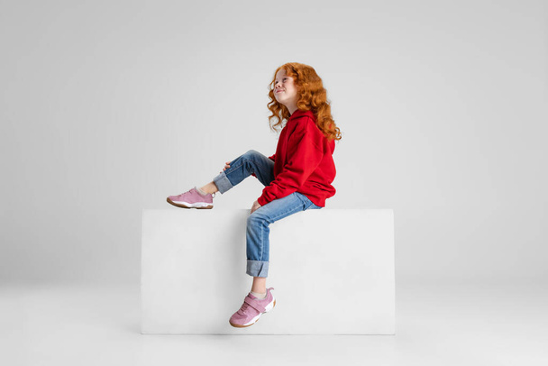 Retrato de la pequeña chica rizada de pelo rojo caucásica soñando mirando hacia arriba aislada sobre fondo gris del estudio. Vista lateral - Foto, Imagen