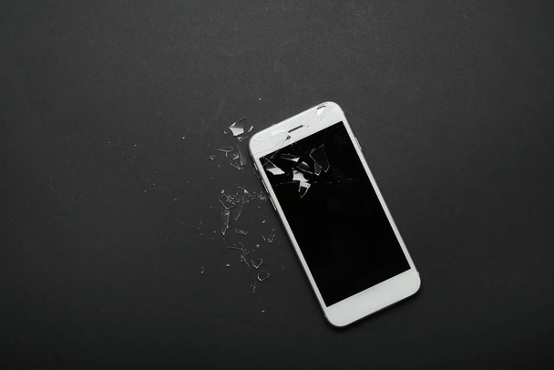 Handy mit zerbrochenem Bildschirm und Glassplittern auf dunklem Hintergrund - Foto, Bild