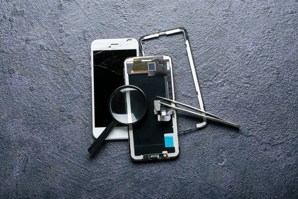 Téléphone portable démonté, pince à épiler et loupe sur fond sombre - Photo, image
