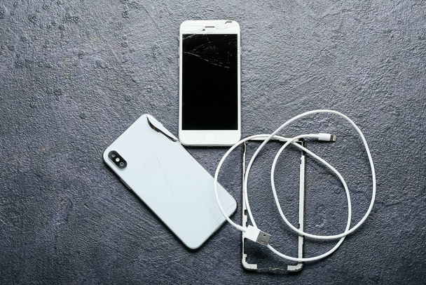 Téléphones portables cassés et cordon de charge sur fond sombre - Photo, image