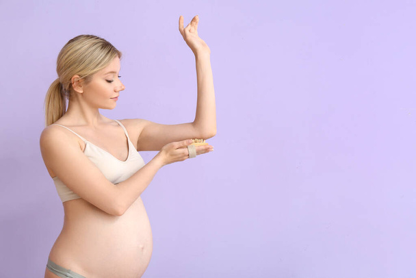 Bella giovane donna incinta con spazzola da massaggio su sfondo di colore - Foto, immagini