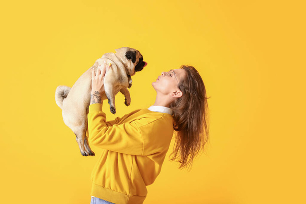 Young woman with cute pug dog on yellow background - 写真・画像