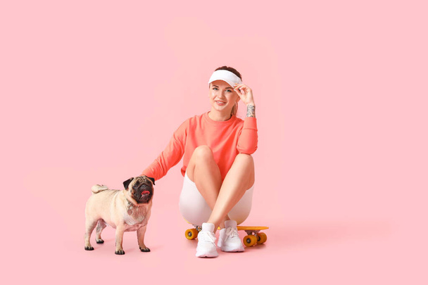 Молодая спортивная женщина с милым мопсом на розовом фоне - Фото, изображение