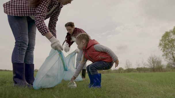 Volunteer happy family collects plastic trash in bags, teamwork, little girl helps adults in the fight for environmental protection, eco, kid with mom clears land from landfill, charity work - Photo, Image